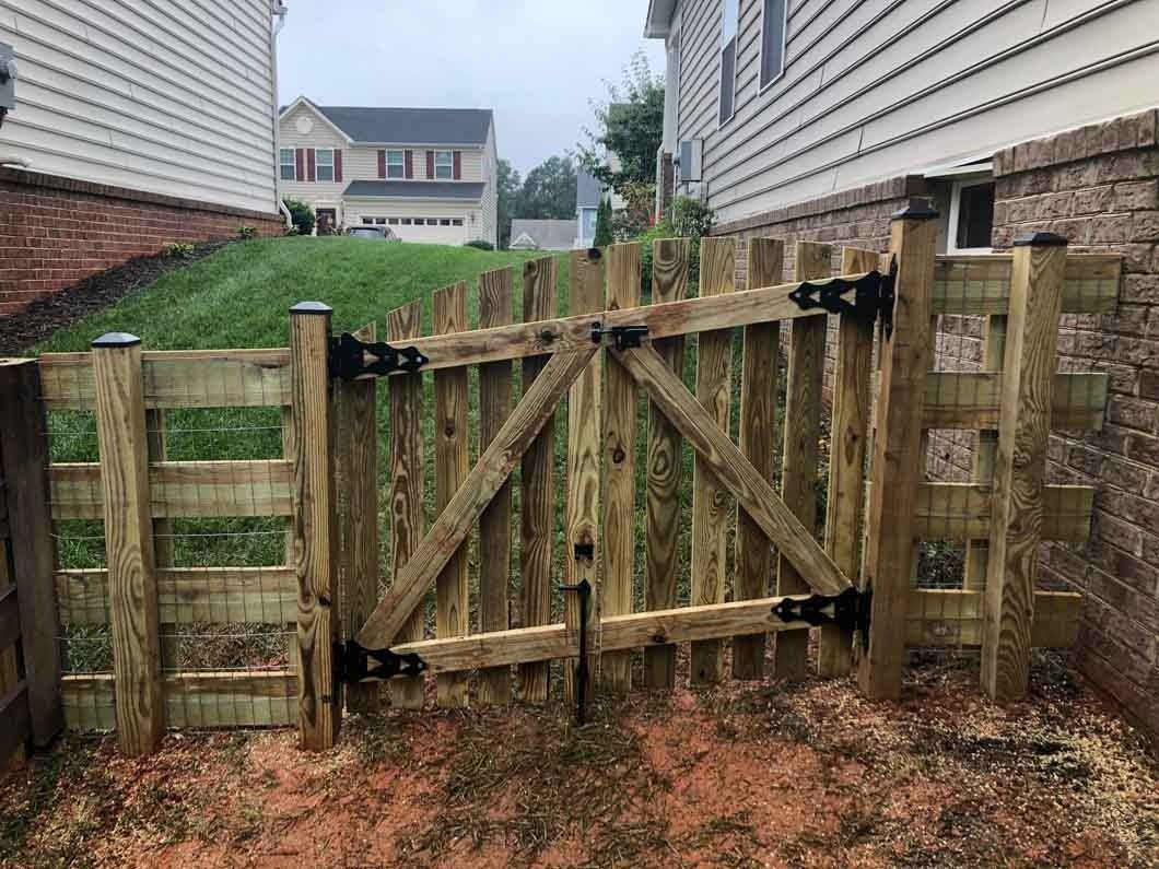 Wooden gate in a backyard, with a house visible in the background on a cloudy day.