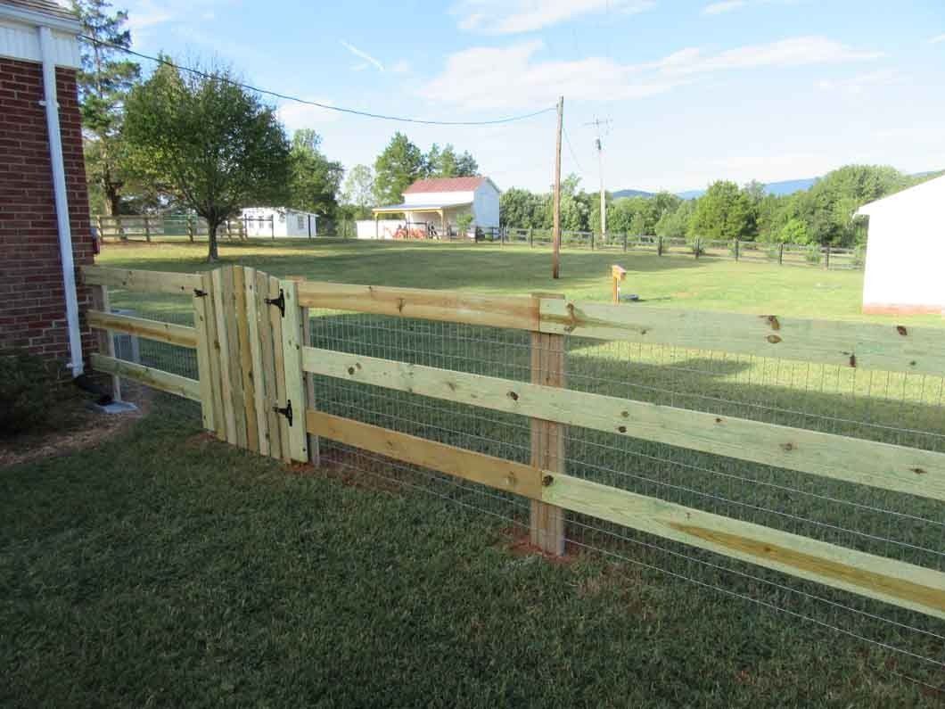 Wooden fence with a gate, in front of a green yard, near a white building, sunny day.