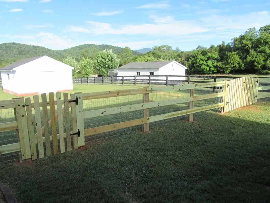Wooden fence with gate in grassy yard, two white buildings in background, mountains in the distance.