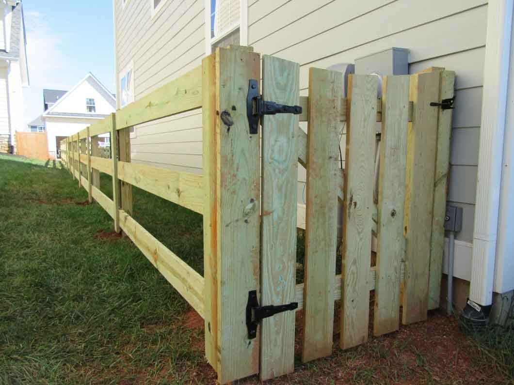 Wooden fence with a gate, green grass, and a beige house in the background.