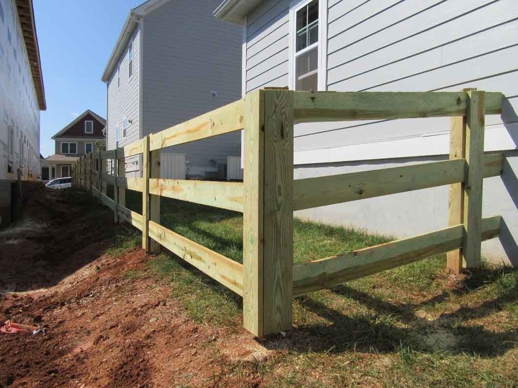 Wooden split-rail fence alongside a house and a dirt path; sunny day.