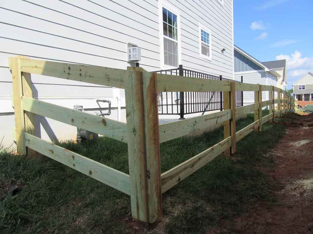 Wooden split-rail fence near a house with gray siding. The fence is made of light brown wood and is set in the grass.
