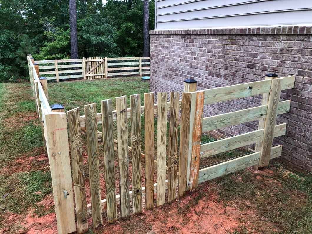 Wooden fence surrounds a yard, connected to a brick wall. A small gate is open.