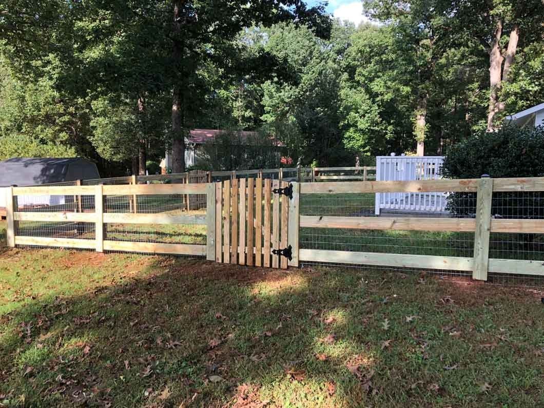 Wooden fence with gate in a yard; trees in the background.