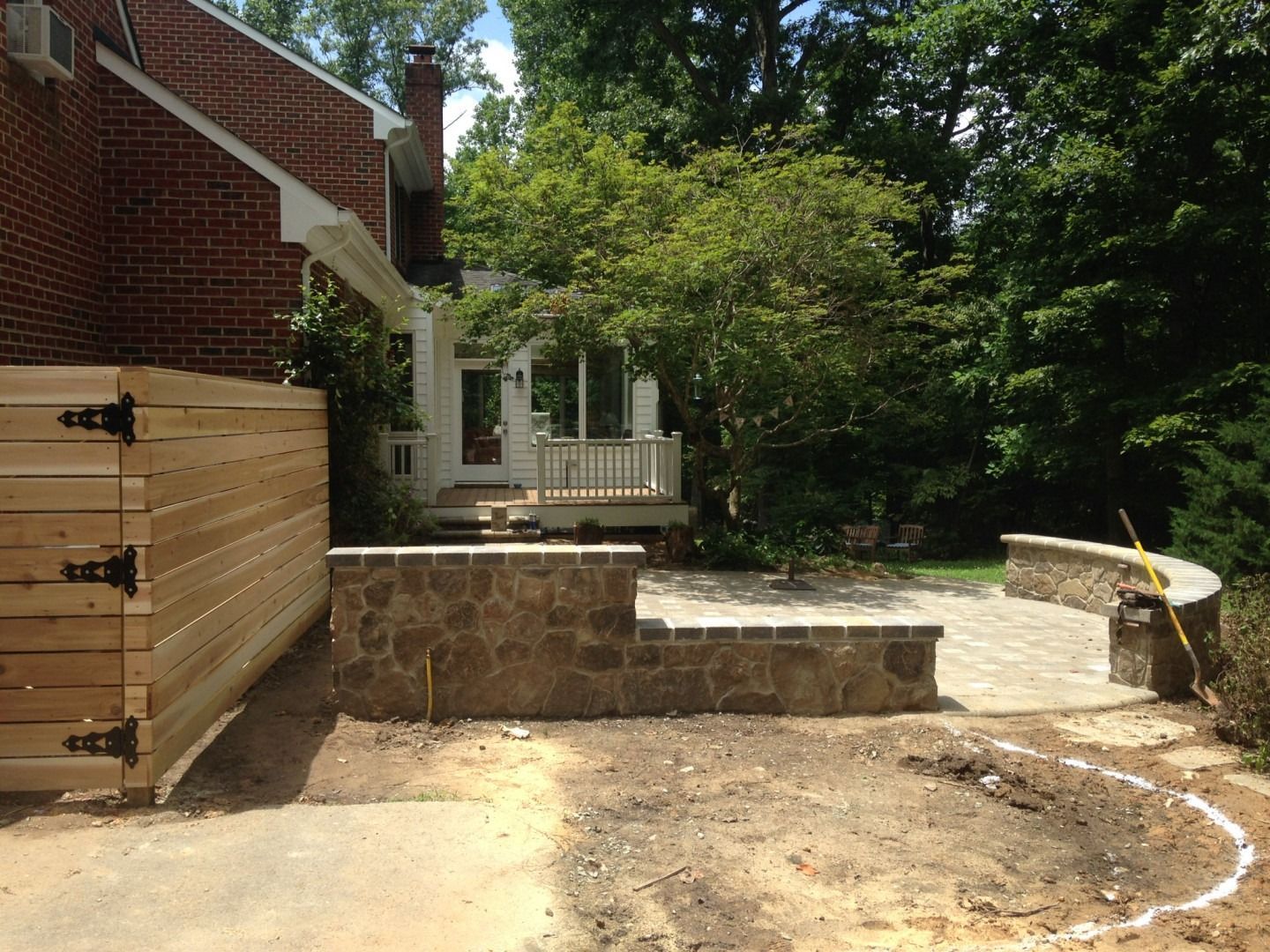 A partially constructed backyard patio with stone walls, wooden fence, and house in the background.