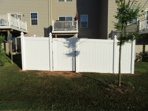 White vinyl fence in a backyard setting, adjacent to a multi-story building.