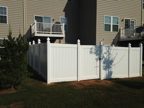 White vinyl fence surrounding a backyard, with a gate and a building in the background.