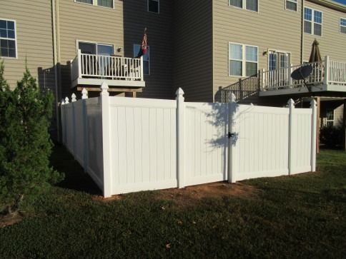 White vinyl fence enclosing a grassy yard, with a gate and two-story building in the background.