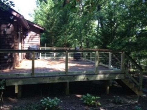 Wooden deck with cable railing and steps leading to a cabin nestled in a wooded area.