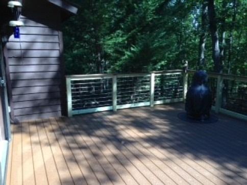 Deck with brown wood-look flooring, metal railing, and a black owl statue in a wooded setting.