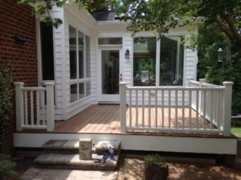 White deck with railings attached to a sunroom with large windows, steps down to a brick patio, and a potted plant.