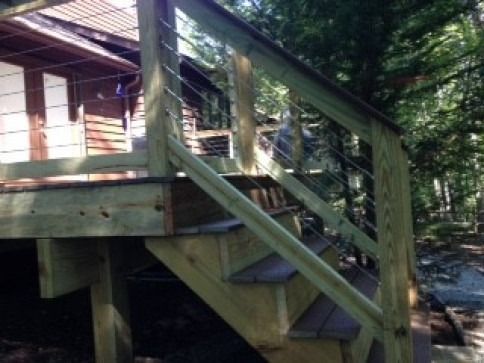 Wooden deck with stairs, featuring cable railings, surrounded by trees.