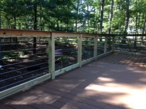 Deck with wooden railing and wire fencing in a wooded area.