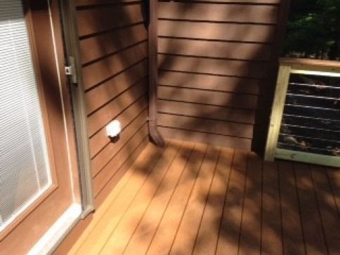 Corner of a brown wooden deck with a door, siding, gutter, and a solar panel.