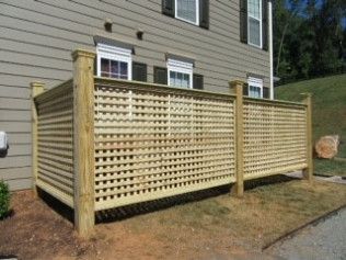 Wooden lattice fence in front of a tan building with windows, on a grassy patch.