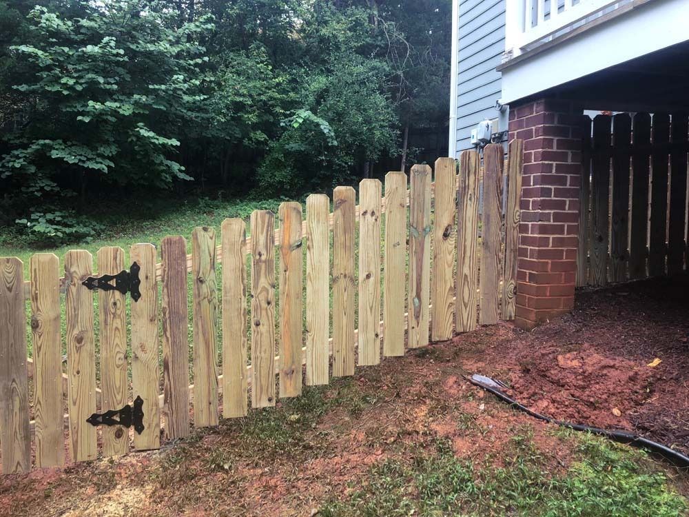 Wooden fence with black hinges, next to a red brick column and a house.
