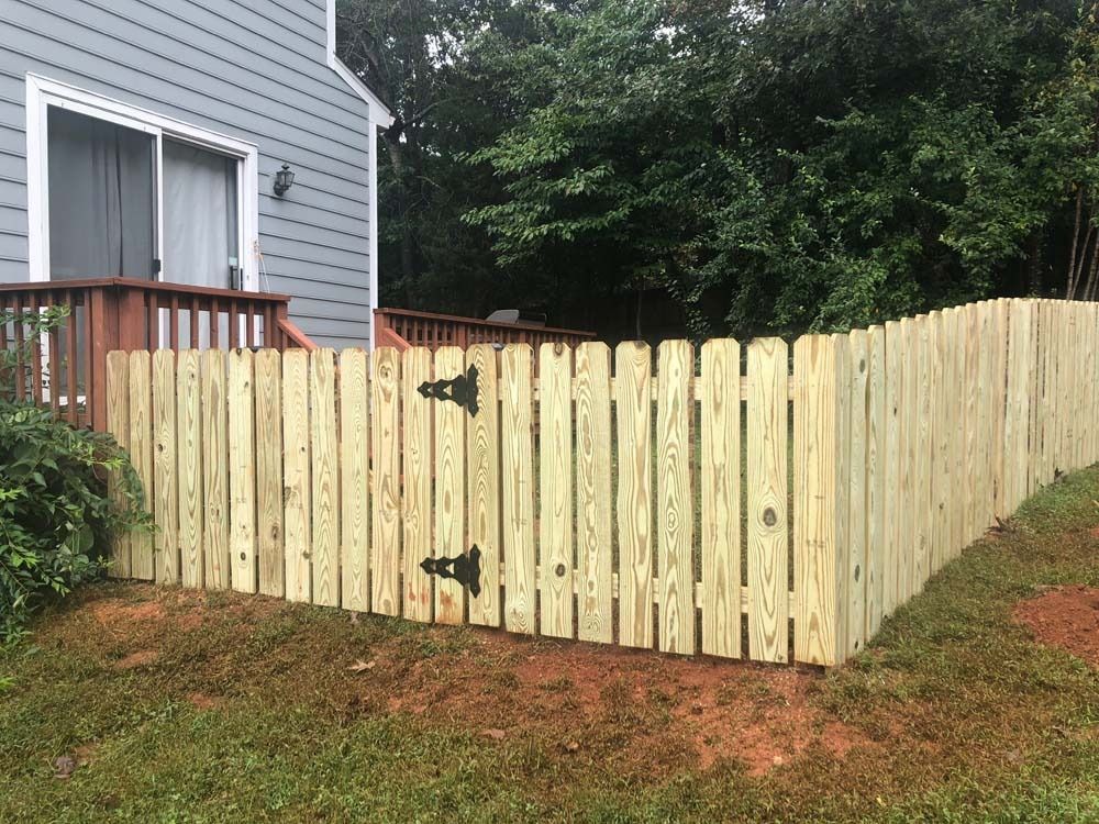 A wooden fence encloses a backyard with a deck, gate, and trees. The fence is made of light wood.