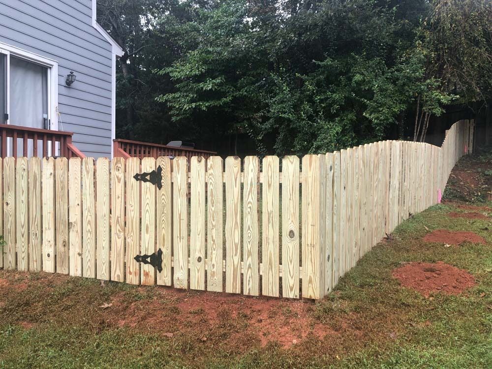 Wooden fence with a gate, in front of a house, and grassy yard.