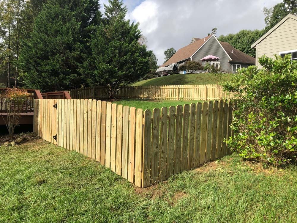 Wooden picket fence surrounding a grassy yard, with a house in the background.
