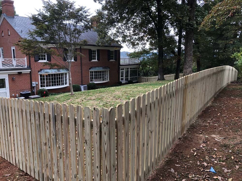 Wooden picket fence in front of a brick house with a sloping lawn.