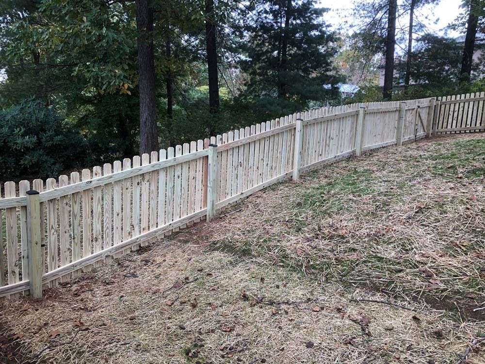 Wooden picket fence curving along a grassy hill, with trees in the background.