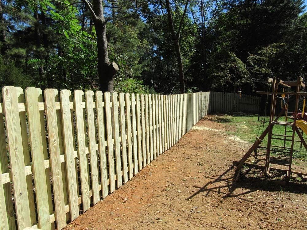 Wooden picket fence in a backyard, partially surrounding a playground, against a backdrop of trees.