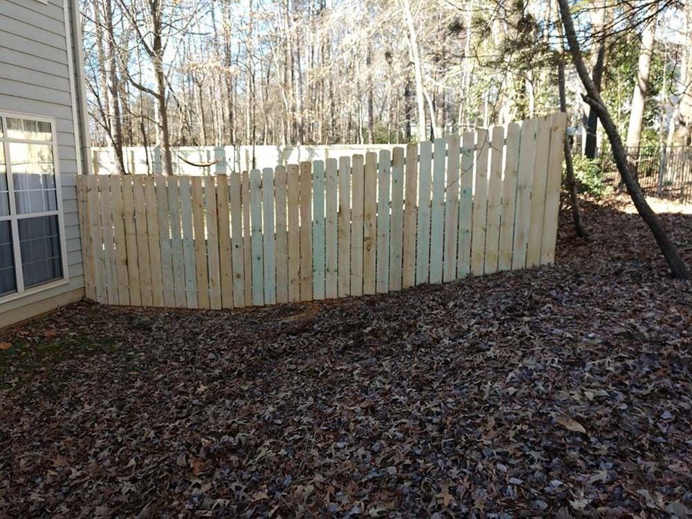 Wooden fence curved around a backyard, with a house on the left and trees in the background.