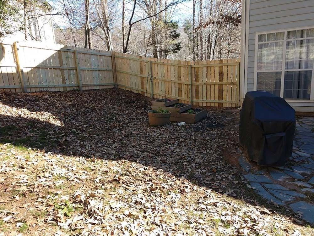 Backyard with a wooden fence, leaves, and a grill covered with a black tarp.