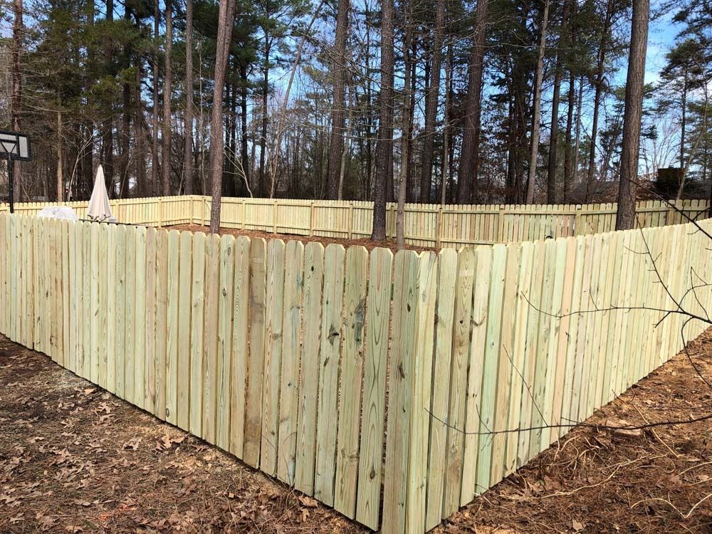 Wooden fence surrounding a yard in a wooded area, trees in the background, daytime.