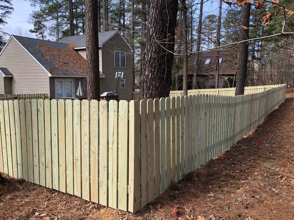 Wooden fence surrounding a house in a wooded area; tan fence, brown leaves.