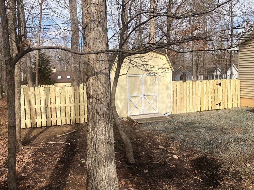 Light yellow shed with fence in a wooded area.