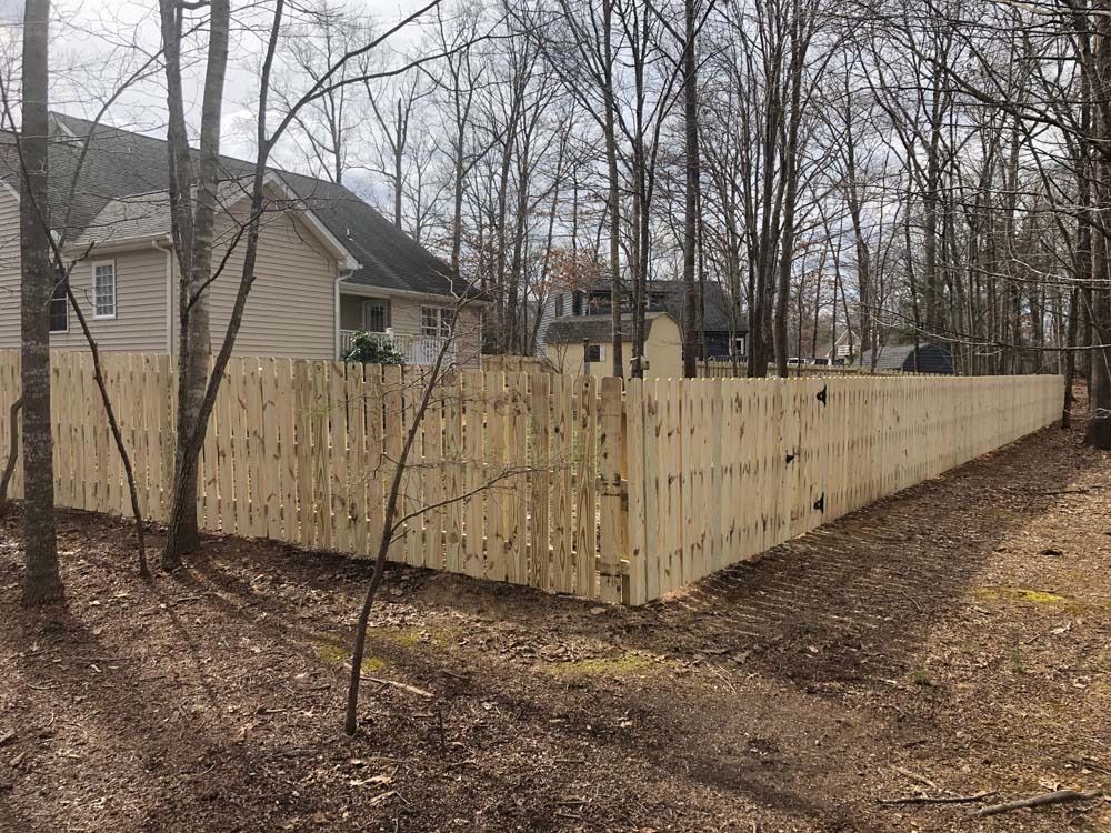 A wooden fence surrounds a yard with a house visible in the background, set amidst trees.