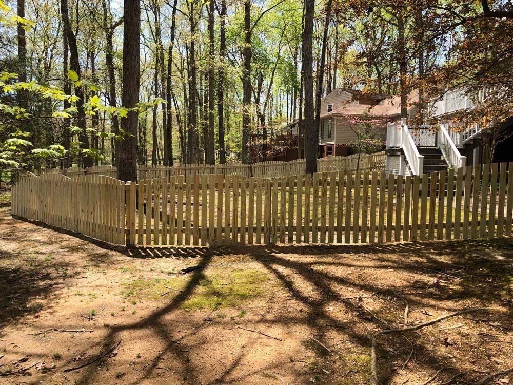 Wooden picket fence in a wooded area, protecting a grassy yard from the surrounding trees and houses.