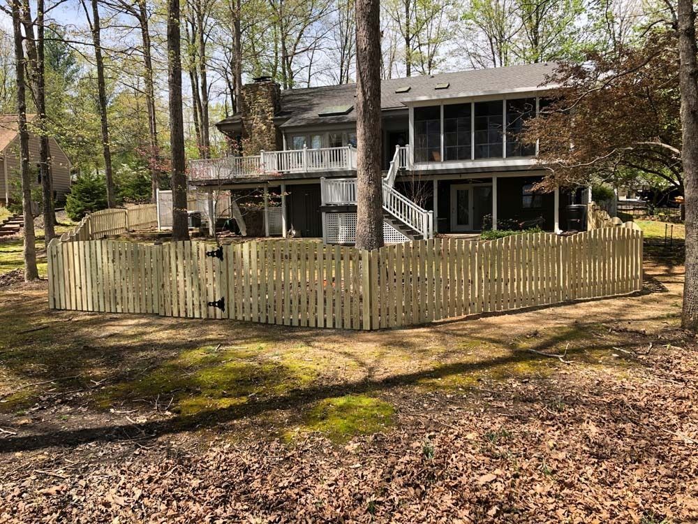 Wooden fence surrounding a two-story house with decks. Trees and foliage surround the property.