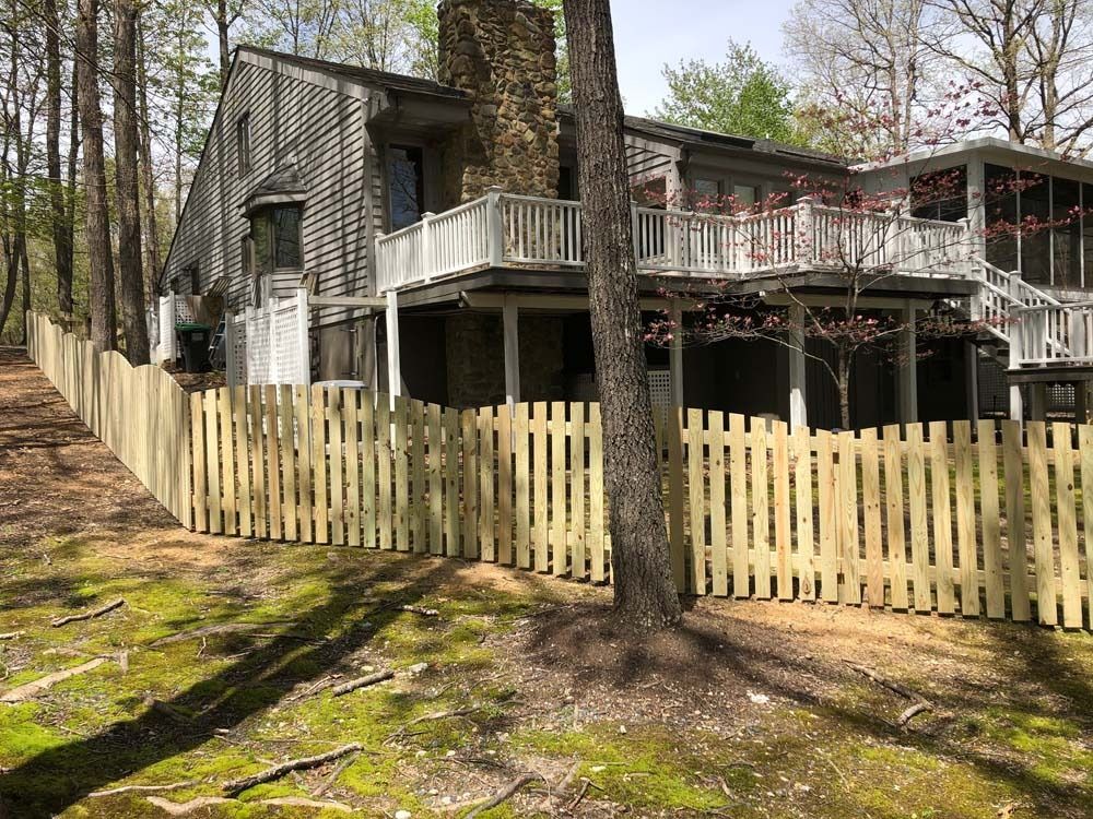A wooden picket fence surrounds a two-story house in a wooded area.