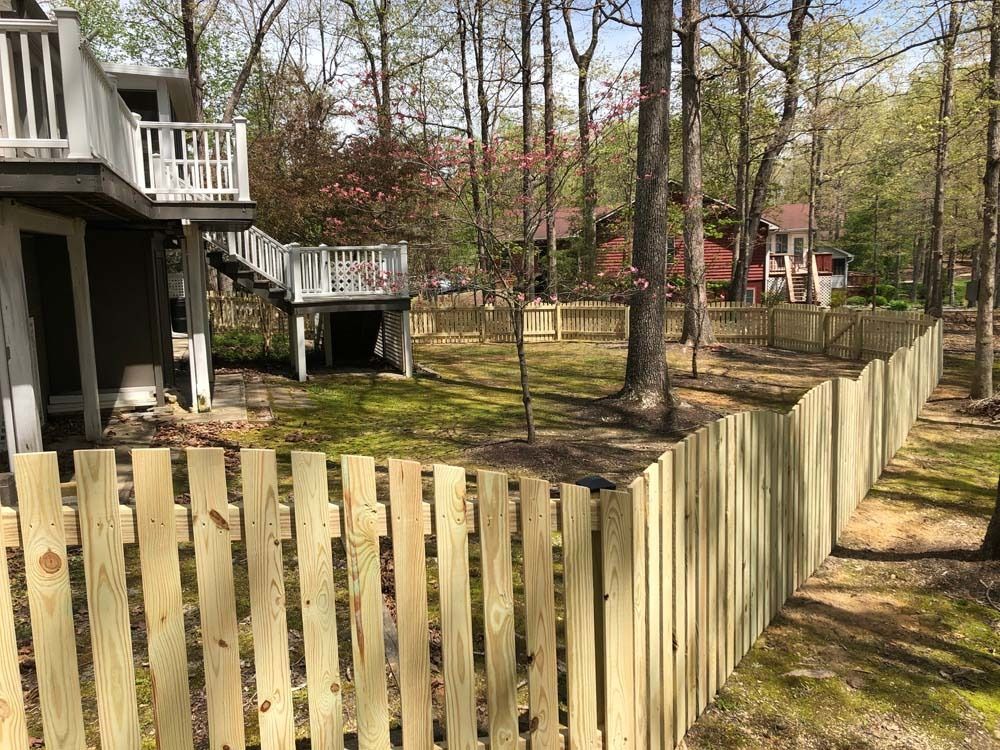 Wooden fence around a backyard with a house, deck, and trees in a sunny setting.