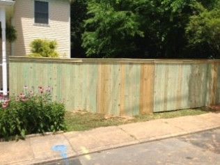 Green wooden fence in front of a house, with grass and a sidewalk.