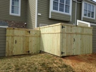 Wooden enclosures against a building, likely for utilities. Fencing is light wood, with doors and black hardware.