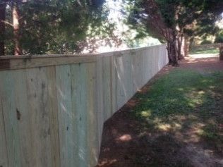Wooden fence alongside a grassy area, trees in the background.