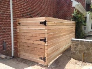 Wooden enclosure with black hinges, next to a brick wall.