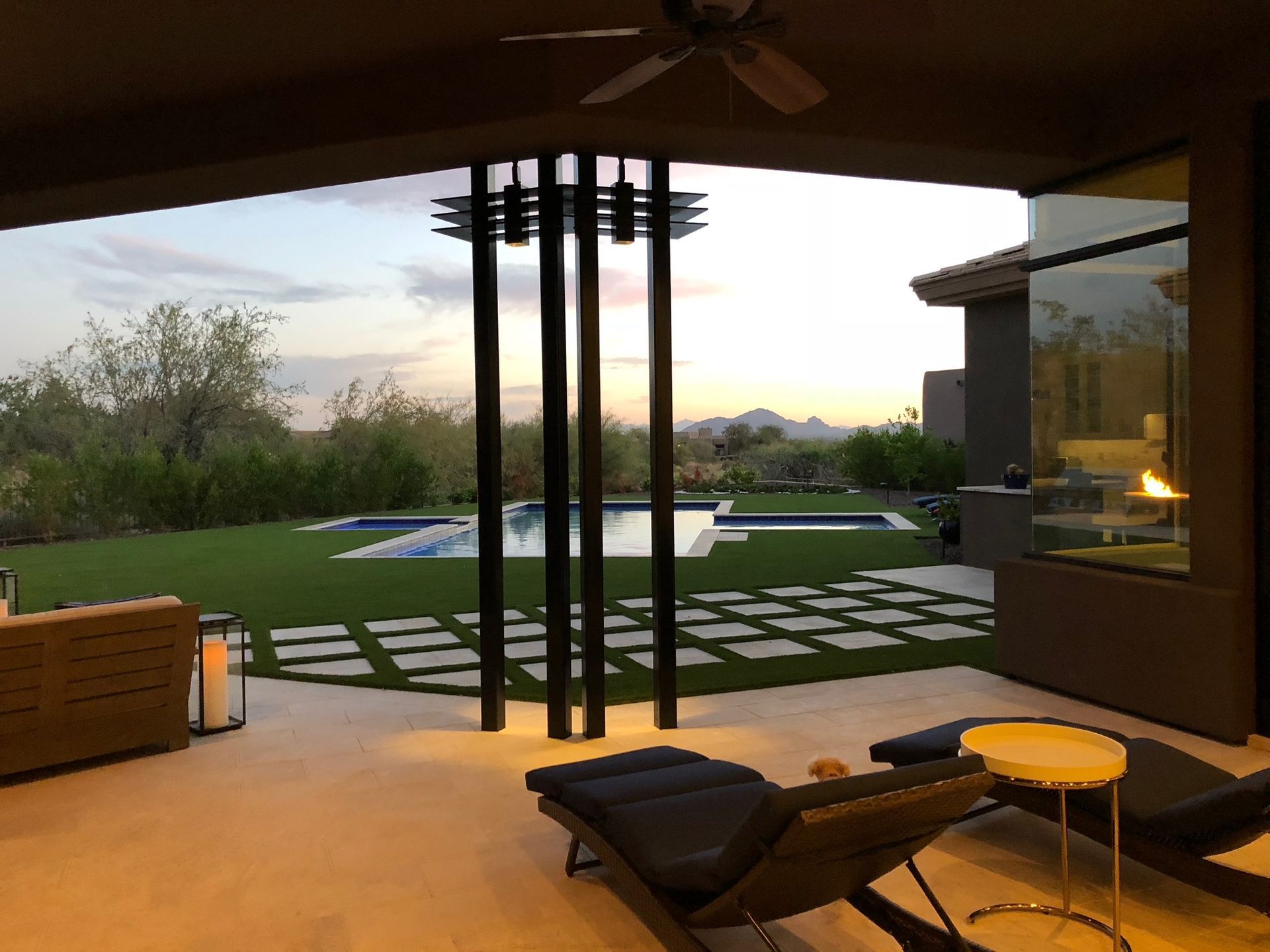 A patio with chairs and a ceiling fan overlooking a swimming pool.