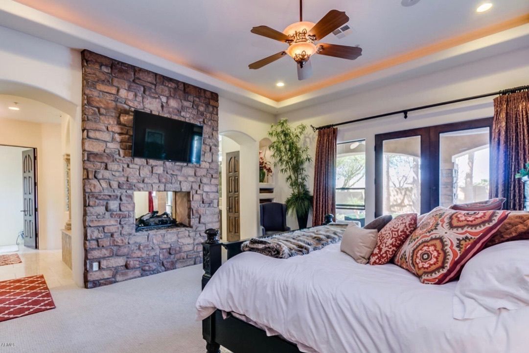 A bedroom with a bed , fireplace , television and ceiling fan.
