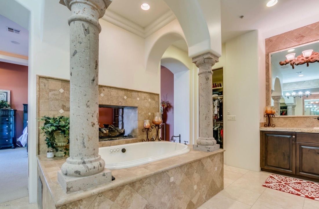 A bathroom with a large tub surrounded by columns and a mirror.