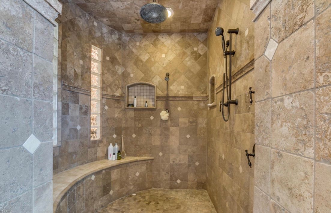 A large tiled shower with a bench and a window.