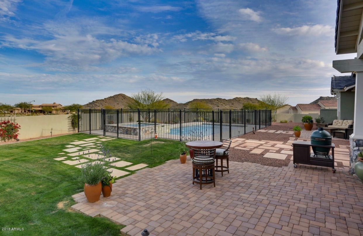 There is a patio with a table and chairs and a pool in the background.