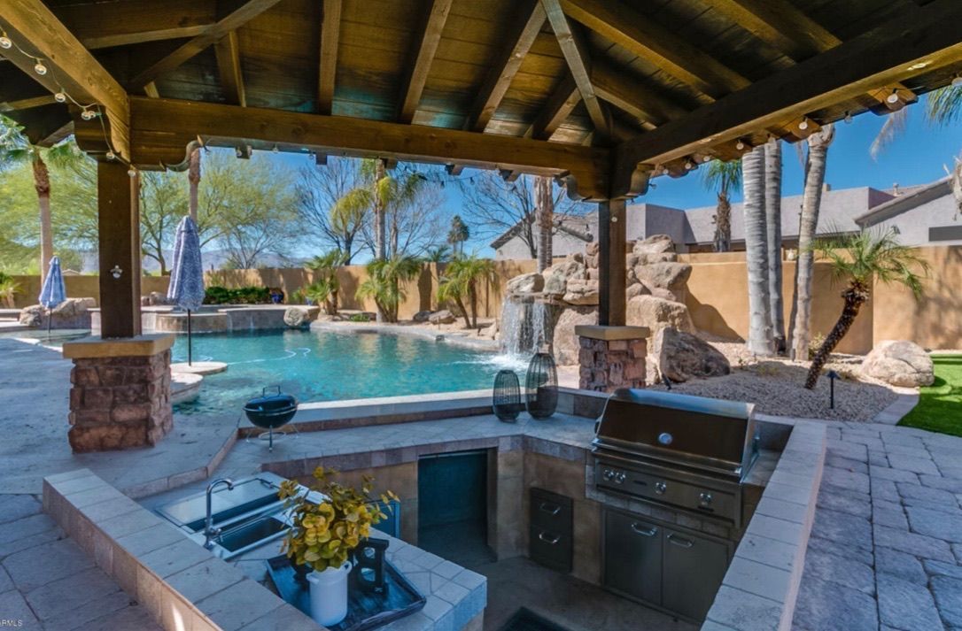 A patio with a grill and a pool under a gazebo.