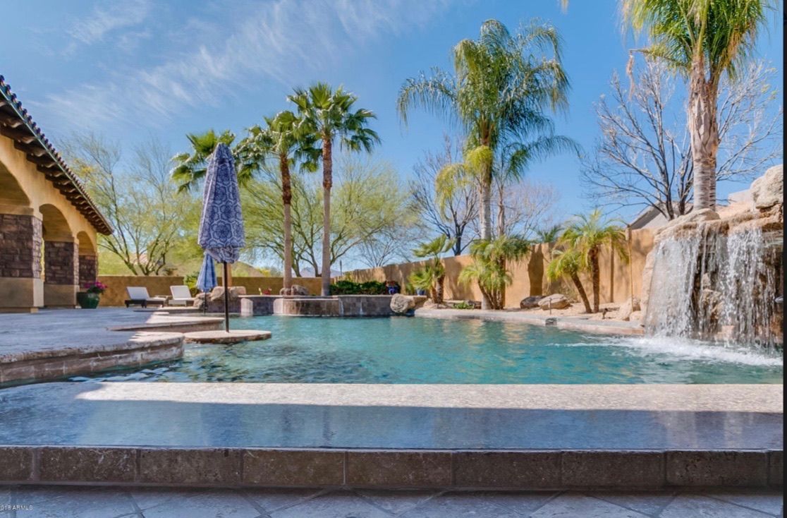 A large swimming pool with a waterfall and palm trees in the background.