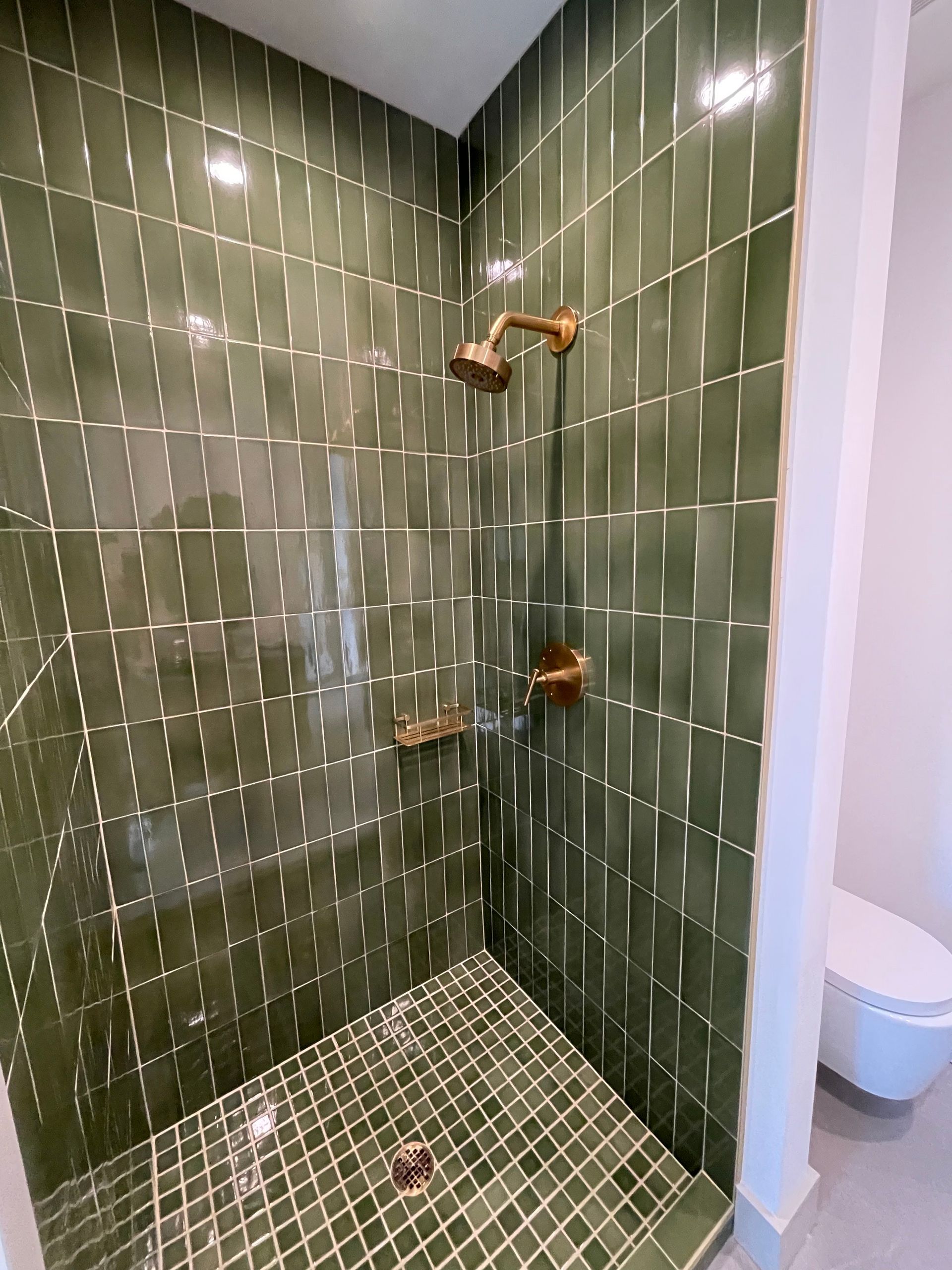 A bathroom with green tiles and a walk in shower.