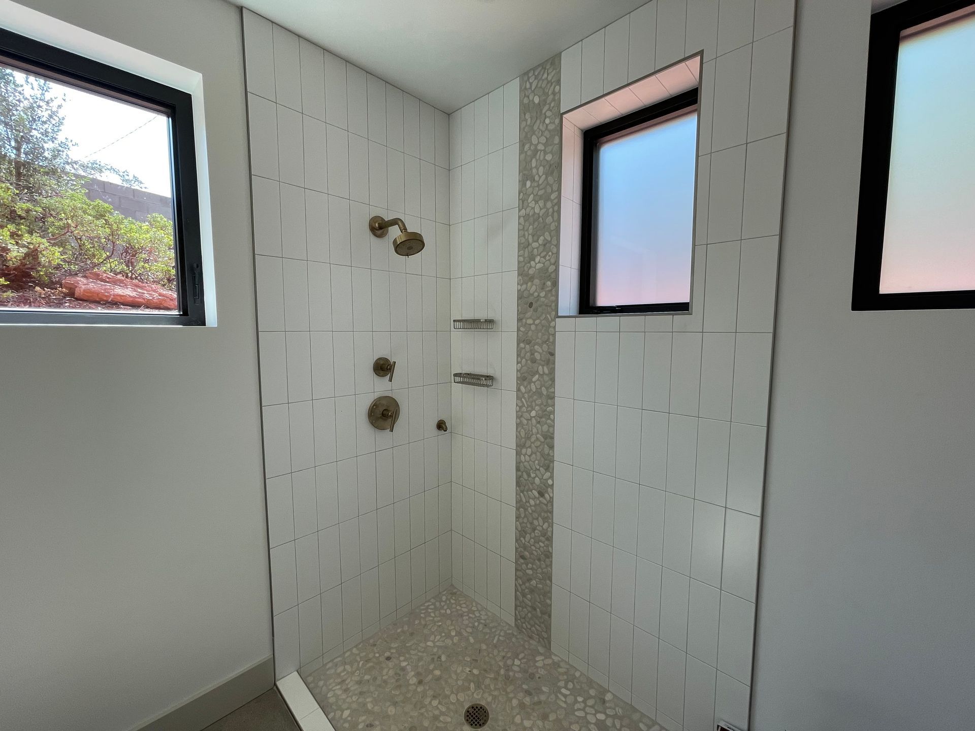 A bathroom with a walk in shower and two windows