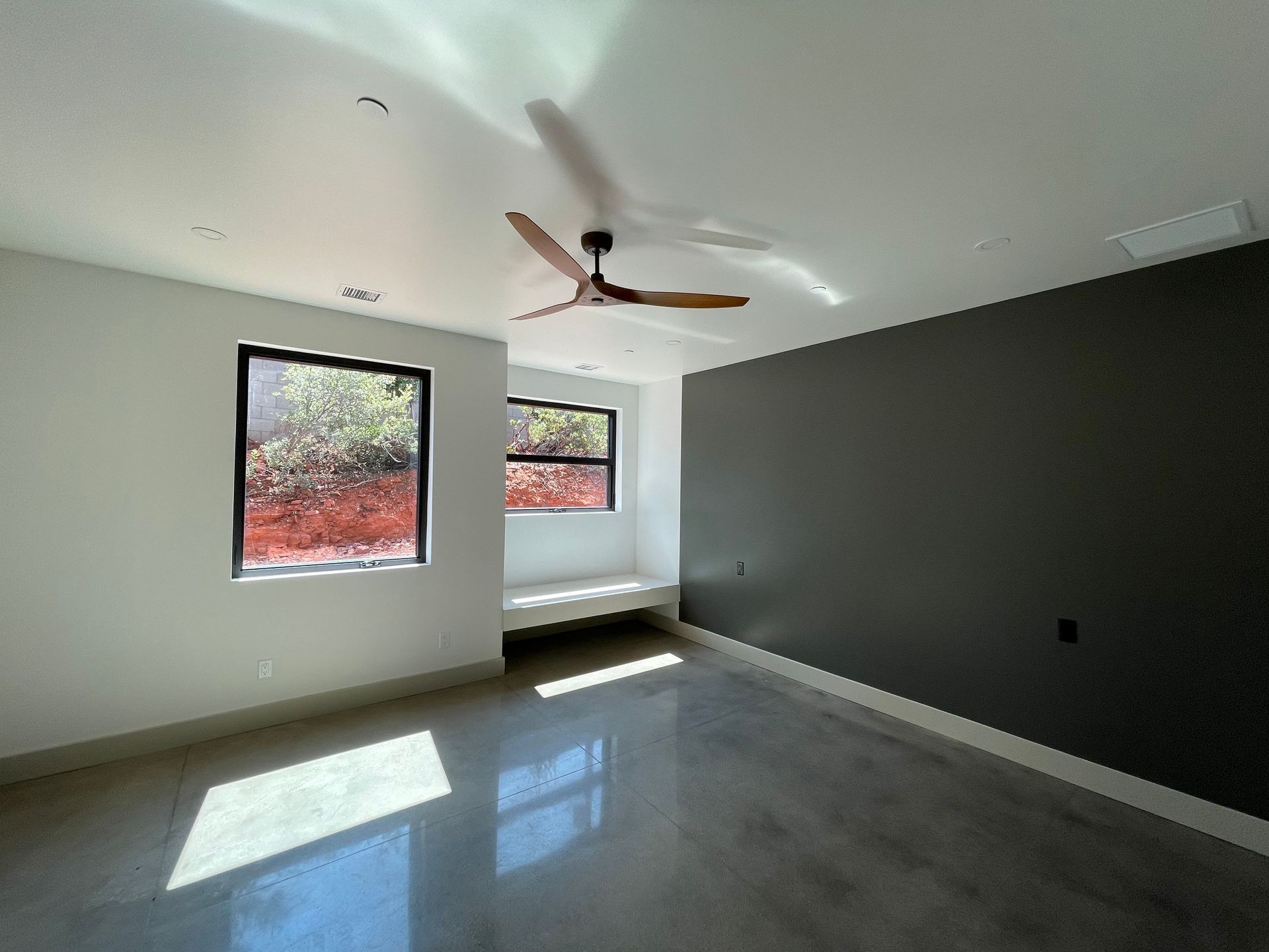 An empty room with a ceiling fan and two windows.